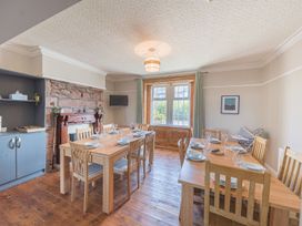 A dining room with two wooden tables and chairs a fireplace and a window with curtains at 1 Cleator Gate in Cleator