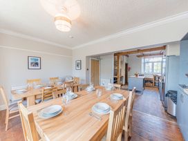 A dining area with wooden tables and chairs set with plates and glasses next to a kitchen with wooden beams and a large window at 1 Cleator Gate in Cleator