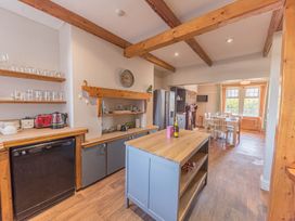A kitchen with wooden beams wooden countertop cabinets an island fridge and a dining table at 1 Cleator Gate in Cleator
