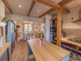 A kitchen with wooden beams and an island table with a bottle and box on it and a dining area with tables and chairs in the background at 1 Cleator Gate in Cleator