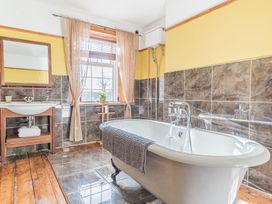 A bathroom with a freestanding bathtub a sink with a mirror and a window with curtains at 1 Cleator Gate in Cleator