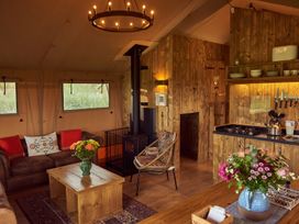 A living area with a brown leather sofa and wooden coffee table with flowers a wooden kitchen with a stove kettle and knives a woven chair and wood burning stove at Pippin lodge in Coxbridge near Glastonbury