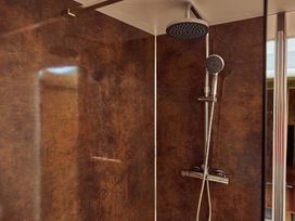 A shower area with a wall-mounted rain shower head and handheld shower on a brown textured wall at Pippin lodge in Coxbridge near Glastonbury