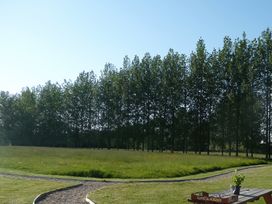 A grassy field with a row of tall trees in the background and a curved gravel path in the foreground with a wooden table and a potted plant at Pippin lodge in Coxbridge near Glastonbury