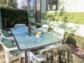 An outdoor dining area with a glass table and chairs at Meadow Island Caravan in Penygroes