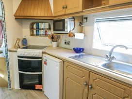 A kitchen with cabinets, sink, stove, and microwave at Meadow Island Caravan Penygroes