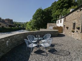 An outdoor seating area with a stone wall and river at Old Post Office Cottage Backbarrow near Newby Bridge