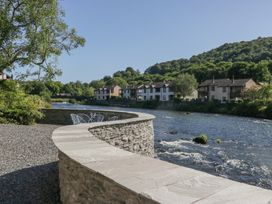 A river with a stone wall and chairs along the water at Old Post Office Cottage in Backbarrow near Newby Bridge