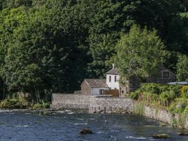 A house near a river with trees and a stone wall at Old Post Office Cottage Backbarrow near Newby Bridge