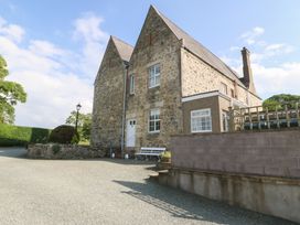 A stone house with multiple windows and a white door next to gravel driveway at Glasfryn in Llandwrog