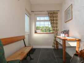 A small entryway with a wooden bench, a window with patterned curtain, and a wooden table with assorted items at Glasfryn in Llandwrog
