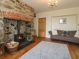 A living room with a stone fireplace and wood stove a basket of firewood a gray sofa and a wooden door at Glasfryn in Llandwrog
