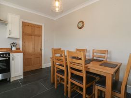 A dining area with a wooden table and six chairs with black seats and a wooden door in a kitchen at Glasfryn in Llandwrog