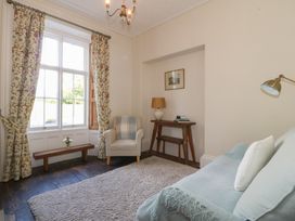 A sitting room with armchair beside a window with floral curtains and a wooden console table with lamp and books at Glasfryn in Llandwrog