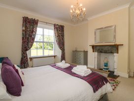 A bedroom with a bed, floral curtains on a window, a chest of drawers, and a fireplace at Glasfryn in Llandwrog