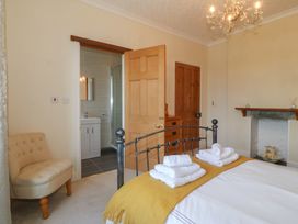 A bedroom with a metal bed frame towels on the bed a beige chair and an open door leading to a bathroom at Glasfryn in Llandwrog