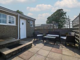 A paved outdoor patio with a white door and windows with wicker chairs and a table at Glasfryn in Llandwrog