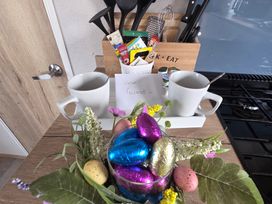 A kitchen countertop with mugs, a note, decorative flowers and plastic eggs at Pines 15 in Porthcawl
