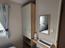 A bedroom with a cabinet, mirror, lamp, and shelf at Pines 15 in Porthcawl