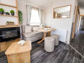 A small dining area with a table set for four next to a cushioned bench and two stools in a room with a wooden coffee table and wall-mounted plants at Lawi39 in Towyn