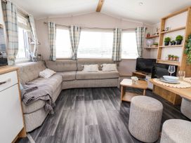 A living room with a beige sectional sofa blue plaid curtains a small wooden table and a TV on a wooden stand at Lawi39 in Towyn
