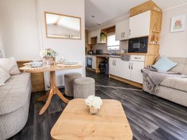 A living area with a small dining table set for four a sofa with cushions and a blanket a kitchen with white cupboards and a microwave at Lawi39 in Towyn