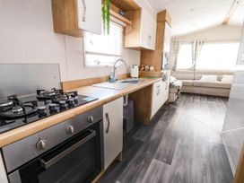 A kitchen with a gas stove oven sink and cabinets leading to a living area with a sofa and windows at Lawi39 in Towyn