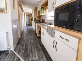 A narrow kitchen with white cabinets a microwave stove sink and hanging plants at Lawi39 in Towyn