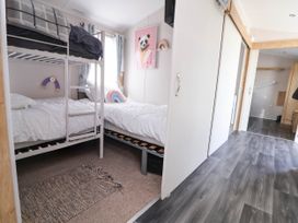 A bedroom with bunk beds and a single bed with white bedding and a rainbow pillow at Lawi39 Towyn