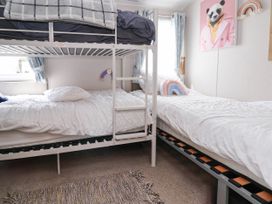 A bedroom with bunk beds and a single bed with white bedding a panda picture on the wall and two rainbow cushions at Lawi39 in Towyn