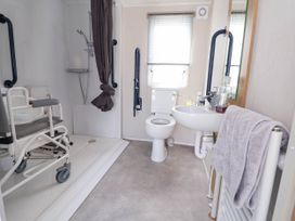 A bathroom with a wheelchair shower chair and grab bars near the shower a toilet and a sink with a towel on a radiator at Lawi39 in Towyn