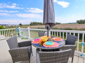 An outdoor deck with a round table set with colorful plates and four wicker chairs with a closed umbrella in the center at Lawi39 in Towyn