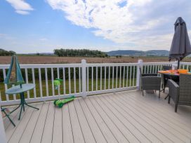 A balcony with a green scooter a small table and chairs with an umbrella overlooking fields and hills at Lawi39 in Towyn