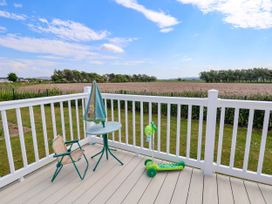 A patio with a small table, umbrella, folding chair and green scooter overlooking a field at Lawi39 in Towyn