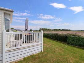 A patio with outdoor furniture and an umbrella next to a grassy yard and fields at Lawi39 in Towyn