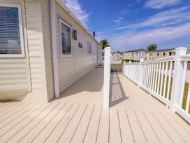 A beige mobile home with a white wooden deck and railing under a blue sky at Lawi39 in Towyn