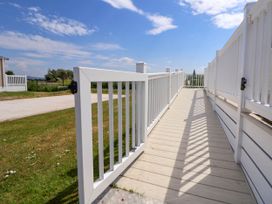 A white wooden ramp with railings leading to a small patio with a table and umbrella at Lawi39 in Towyn
