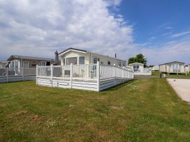 A lawn with multiple small houses and a white fenced porch around one house at Lawi39 in Towyn