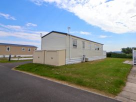 A beige mobile home on a grassy plot next to a paved road at Lawi39 in Towyn