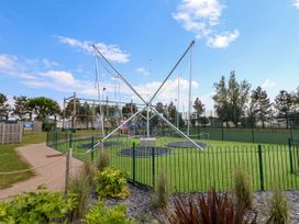 An outdoor trampoline and climbing setup with fencing around it on a grassy area at Lawi39 in Towyn