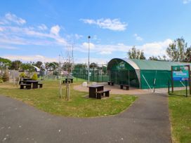 Outdoor area with picnic tables trees and a green tent near a fenced sports court at Lawi39 in Towyn