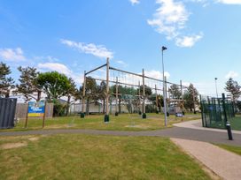 An outdoor ropes course and fenced sports area in a park with trees at Lawi39 in Towyn