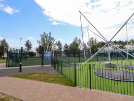 An outdoor sports court with fenced trampolines and a soccer field at Lawi39 in Towyn