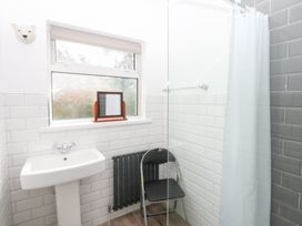 A bathroom with a wash basin, mirror, shower, and chair at Seabreeze in Llandudno