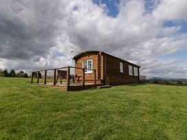 A wooden cabin with deck and bench in a grassy field under cloudy sky at Twilight in Raglan