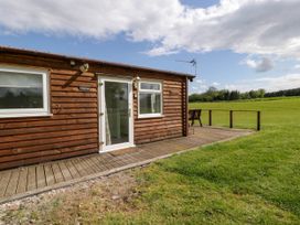 A wooden lodge with windows and a door opening onto a deck overlooking a grassy field at Twilight in Raglan