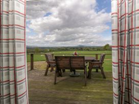 A wooden deck with a table and chairs and a basket of flowers overlooking a green field with sheep and hills in the distance at Twilight in Raglan