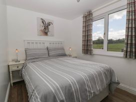 A bedroom with a double bed striped gray bedding bedside tables with lamps and a window with plaid curtains at Twilight in Raglan