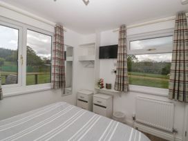 A bedroom with a bed a television two windows with checked curtains and two bedside tables at Twilight in Raglan