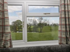 A window with plaid curtains looking out to a grassy field with trees and a pond at Twilight in Raglan